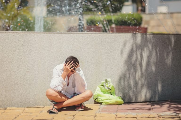 Sad teenager sitting upset near the fountain and holding his head in his hands