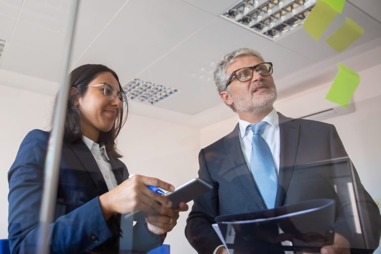 Focused colleagues reading stickers on glass wall and standing