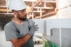 Holding the plasterboard. Young factory worker in grey uniform