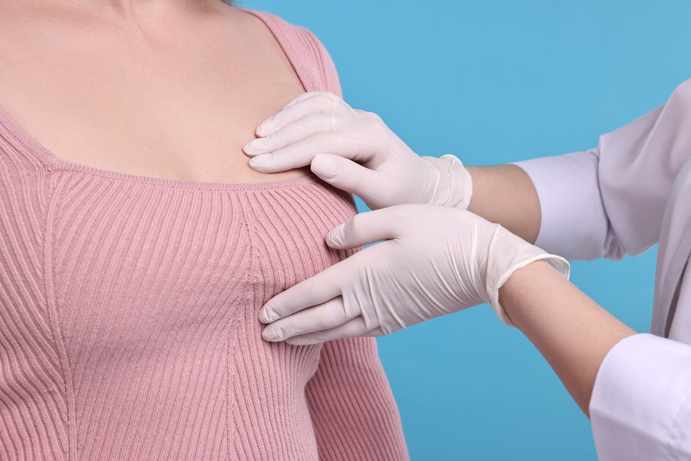Mammologist checking woman's breast on light blue background, cl