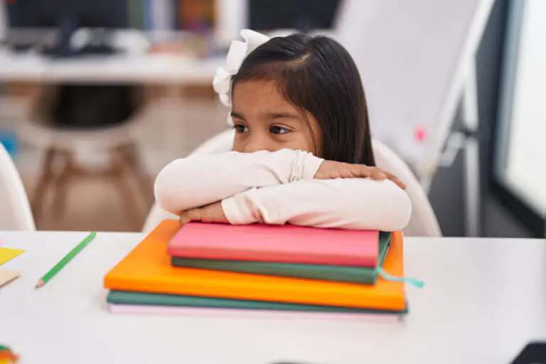 Adorable hispanic girl student smiling confident leaning on book at classroom